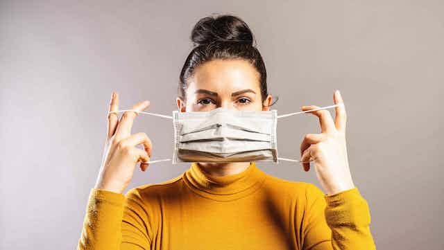 A woman holds a surgical mask across her face.
