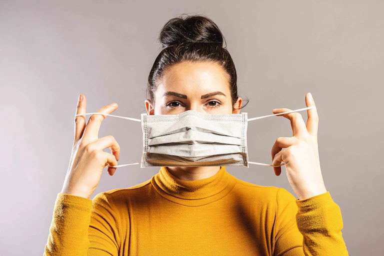 A woman holds a surgical mask across her face.