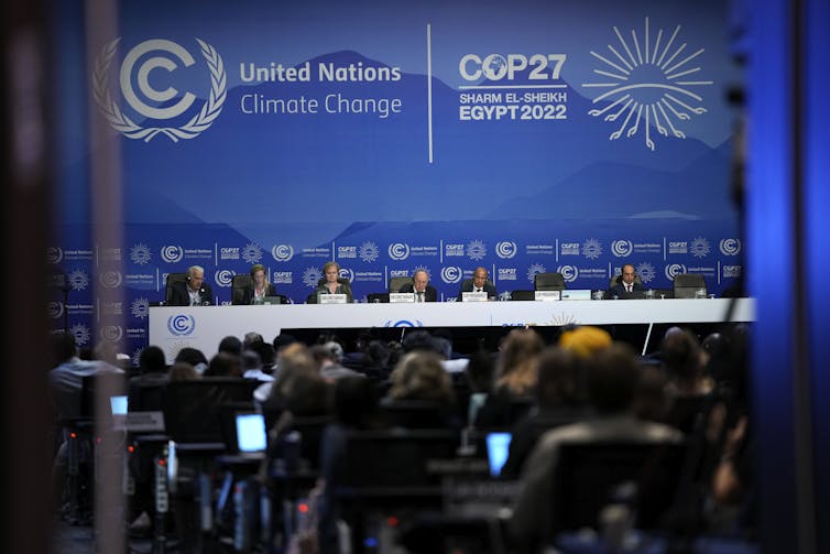 A panel of six people sit behind a long table in front of an audience. Behind the panel, the words 'United Nations COP27' are displayed.