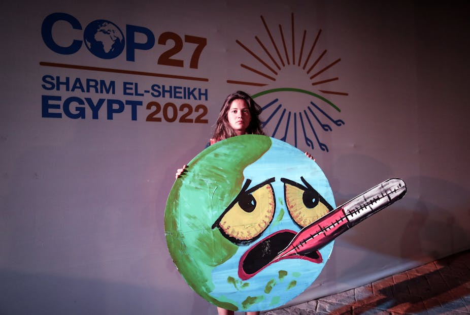 Activist in front of a COP27 sign holds a picture of the Earth with a face, and a thermometer in its mouth.