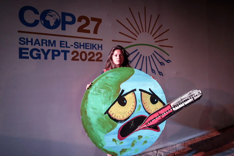 Activist in front of a COP27 sign holds a picture of the Earth with a face, and a thermometer in its mouth.