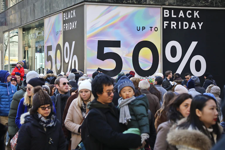 crowds of people, some wearing stocking hats, walk in the street past big black friday signs advertising 50% offf