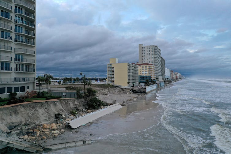 A tall condo building with balconies and erosion almost to the edge of the building