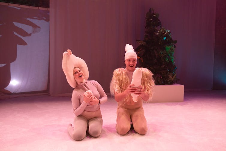 Two people on stage, wearing clothing but pretending to be naked.