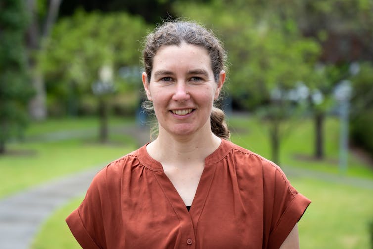 A smiling woman with curly hair looking at the camera with greenery in the background