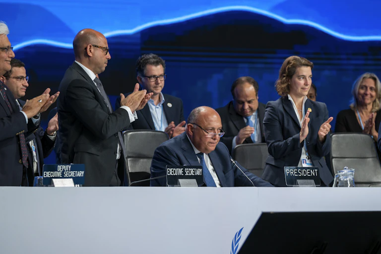 People stand and clap as Shoukry, sitting at the speakers dais, wraps up COP27.