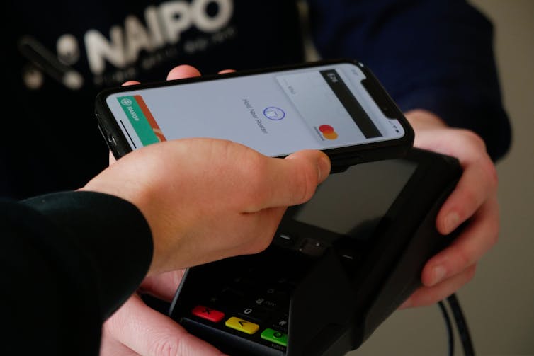 A person holds their smartphone to a contactless payment system