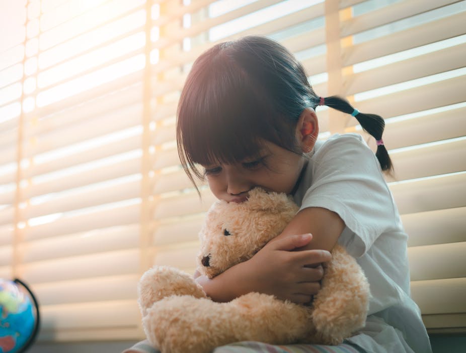 A young girl sadly holding a teddy bear