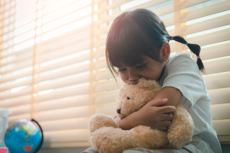 A young girl sadly holding a teddy bear