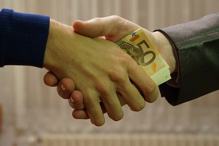 Two men shaking hands with euro banknotes hidden in the hands