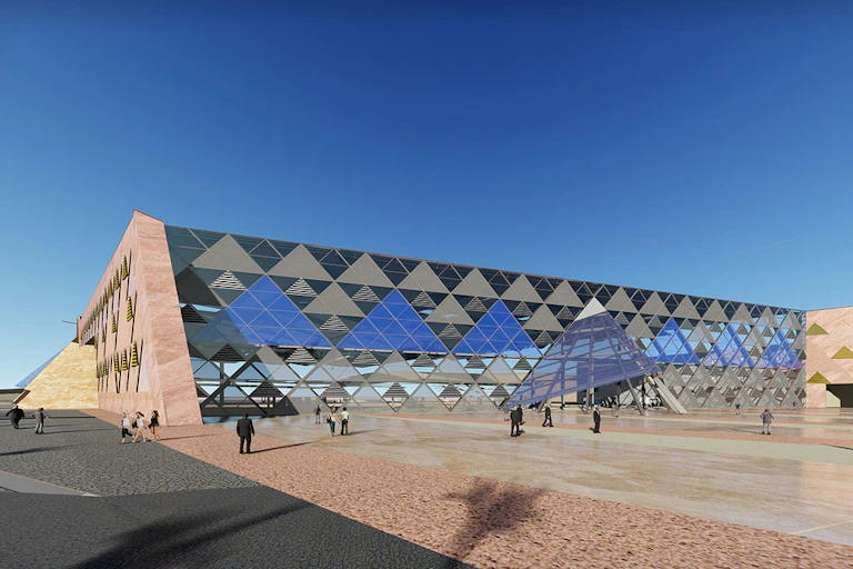 An exterior photograph of the Grand Egyptian Museum against blue skies. The building has mirrored triangular glass covering its exterior, mirroring Egypt's famous pyramids