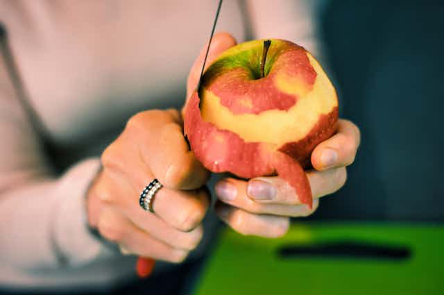 Unas manos pelando una manzana roja con cuchillo.
