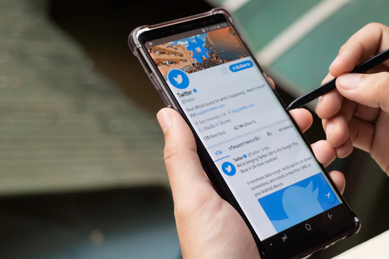 A hand holds a phone showing the Twitter twitter feed