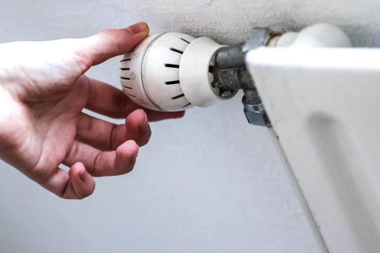 Une main baisse le thermostat d'un radiateur.