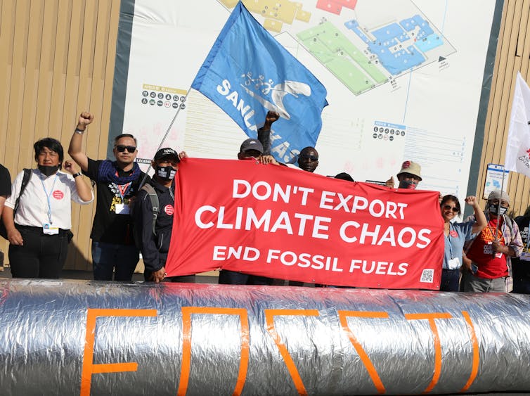 Protesters hold a sign saying 'don't export climate chaos/end fossil fuels' behind a replica pipeline.