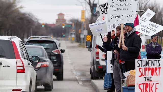 People seen holding strike signs at the side of vehicles going down a street.