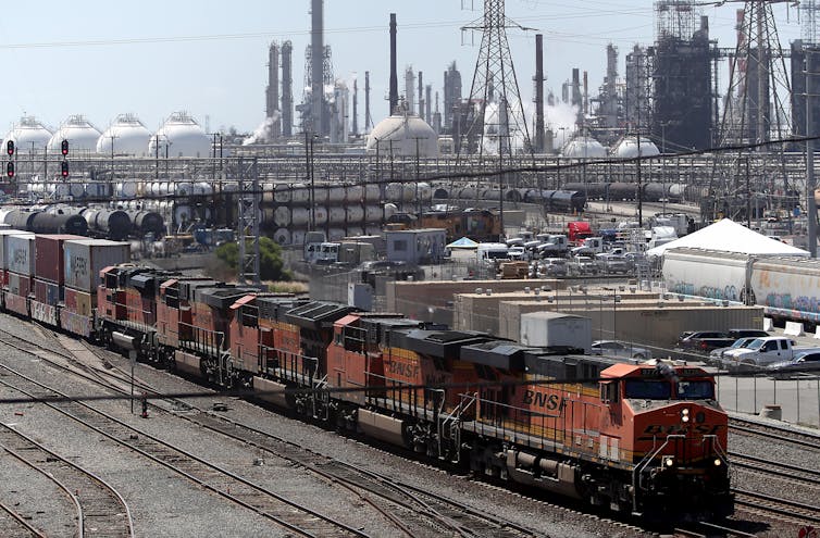 A freight train rolls past an oil refinery.