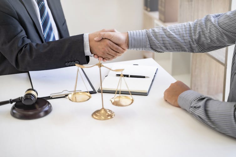 Two men shaking hands after coming to an agreement. A balanced scale is also on the table.