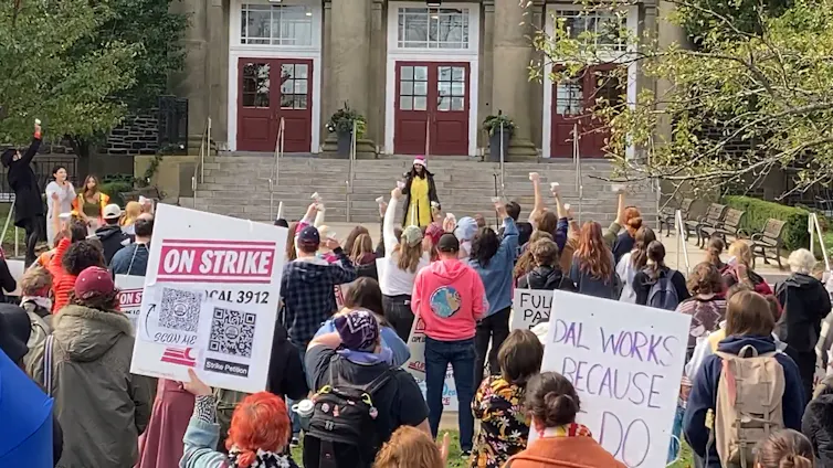 A crowd holding placards seen listening to someone giving a speech.