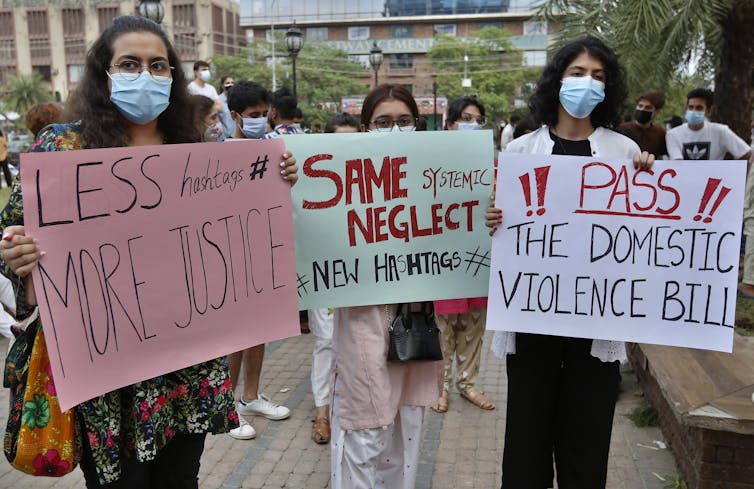 Three women hold placards with messages against domestic violence.