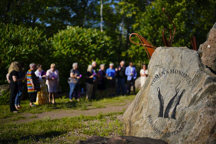 People gather near a rock with the words: women's monument.