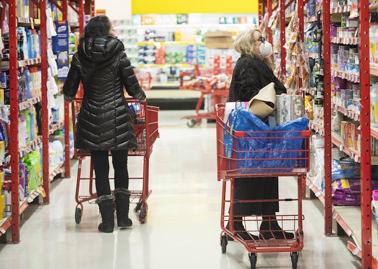 Two women pushing shopping carts down the aisle of a grocery store