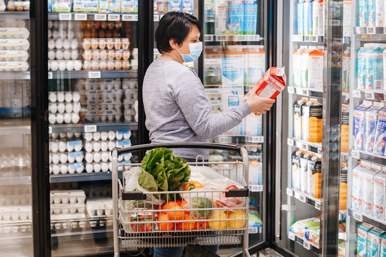 A woman in a mask look at a carton of milk in a grocery store