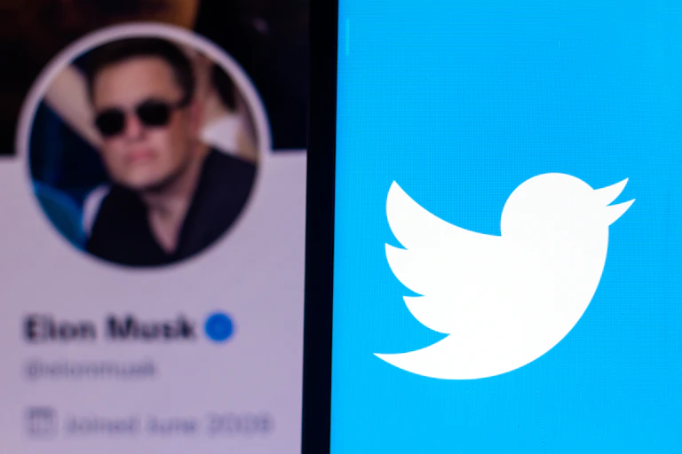 A smartphone with the Twitter logo in the foreground. Behind it is a photo of Elon Musk's Twitter profile.