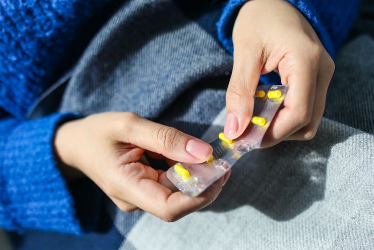 person holding blister pack of yellow capsules