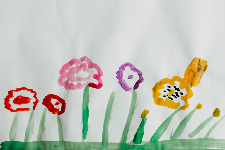 A child's painting of colourful flowers on green grass.