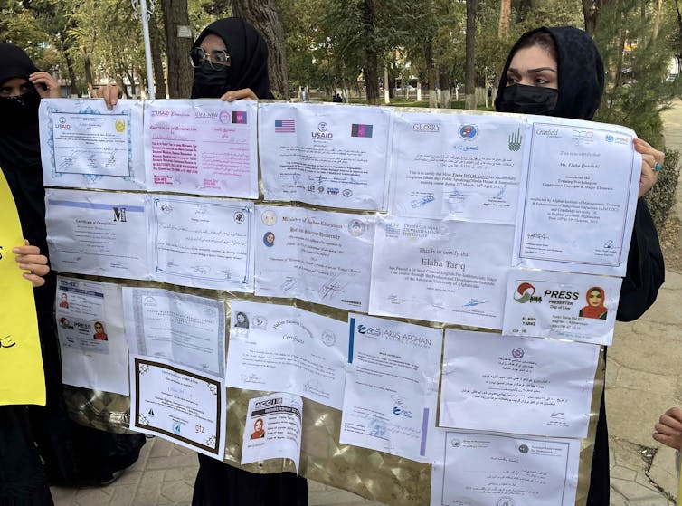 Women wearing the burqa hold up a noticeboard.