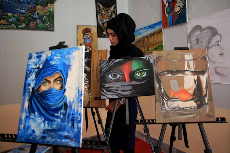 A young woman wearing a burqa displays her artwork.