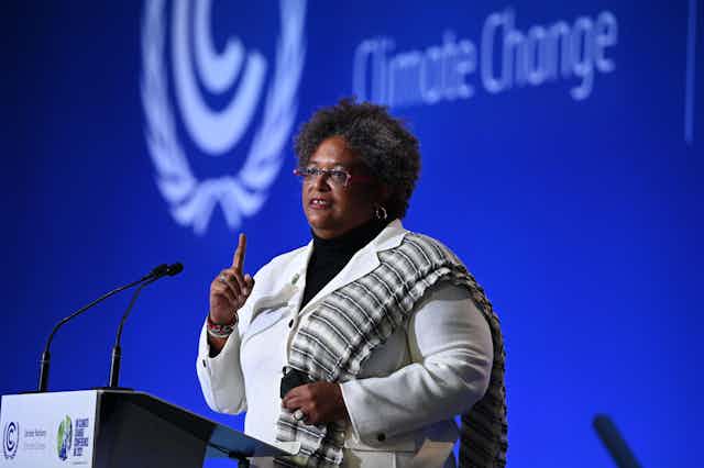 Mia Mottley mid-speech at a lectern in front of a blue background.