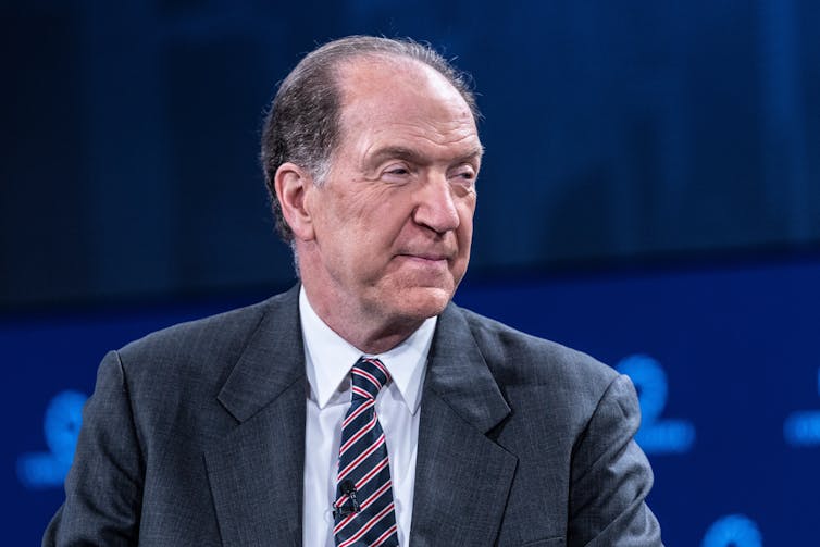 Um homem de terno está de frente para a direita.