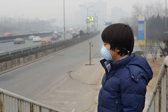 Niño con mascarilla junto a carretera con humo.