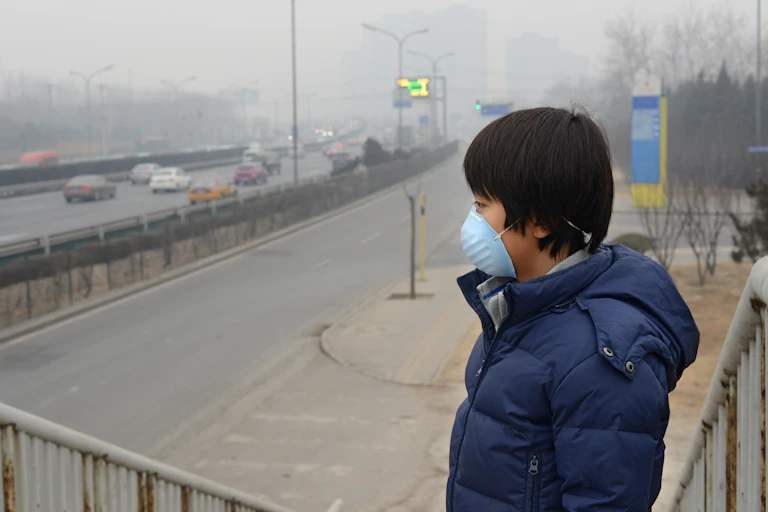 Niño con mascarilla junto a carretera con humo.