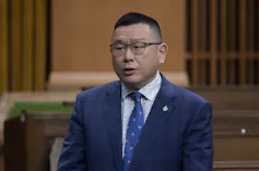 An Asian man in a dark blue suit wearing glasses.