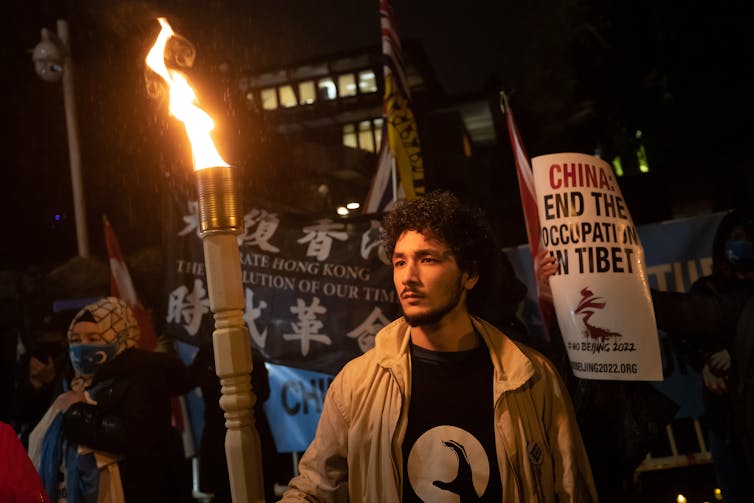 A dark-haired man holds a torch during a night-time protest.