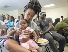 A Black woman sits with a baby on her lap in a government office.