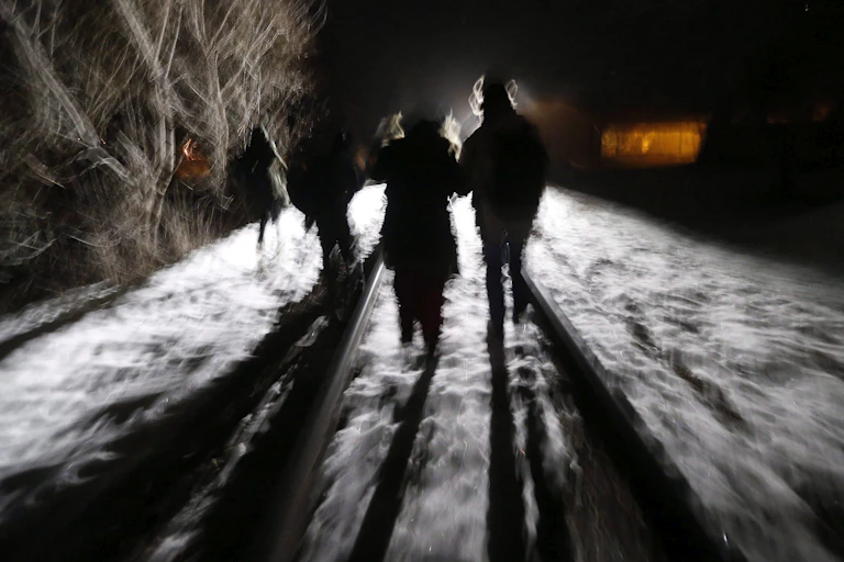 A blurred photo shows the shadows of migrants as they walk along a railroad track in the darkness.