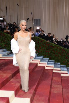 Kim Kardashian on the red steps of the Met Gala, wearing Marilyn Monroe's nude bejewelled Mr President dress. Her hair is slicked back in a bleach blonde bun.