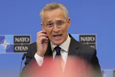 A man holds his hand to his ear piece while speaking into a microphone.