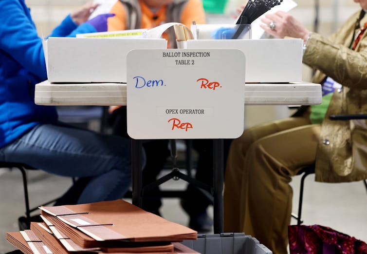 People counting ballots at a table, with signs saying 'Dem' and 'Rep' for each party.