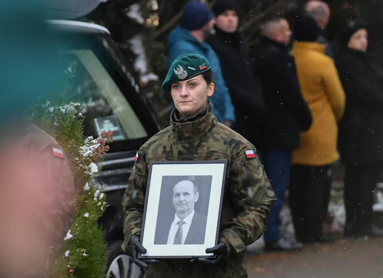 A female guard in uniform holds a black-and-white photo of a middle-aged man.