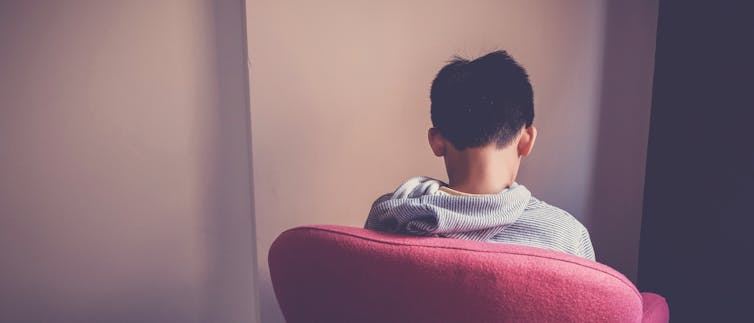 a young person sitting in a red chair with their back to the viewer