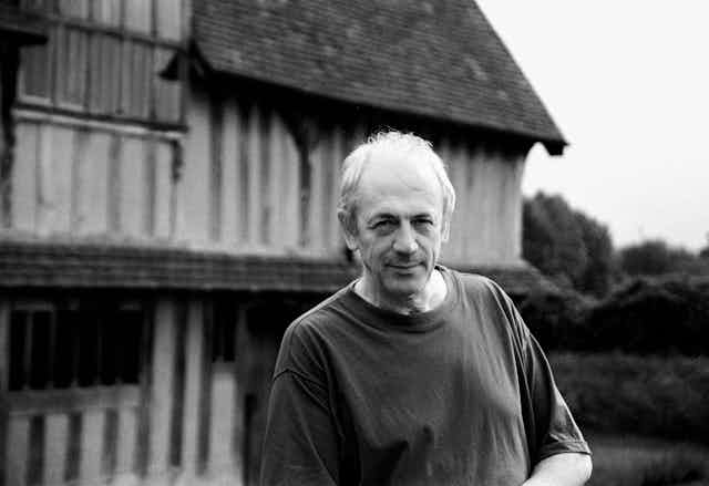 A black and white photo of a man in front of Tudor house.