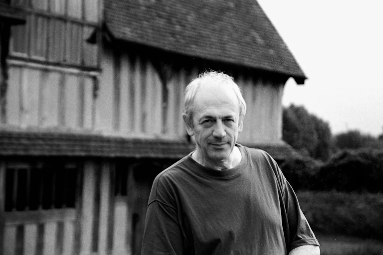 A black and white photo of a man in front of Tudor house.