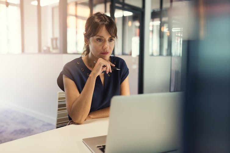 A woman in an office working on a laptop.