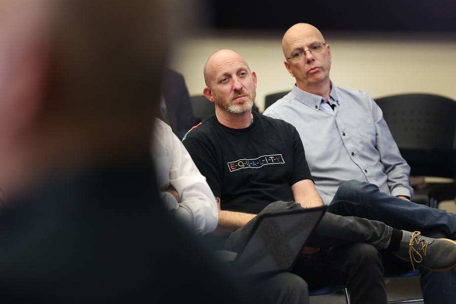 Two white men with bald heads are sitting next to each other with sorrowful expressions on their faces.