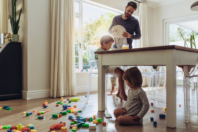 Man wiping dishes while looking after two young children